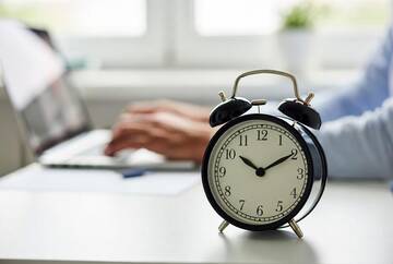 mani che digitano su tastiera con in primo piano una sveglia