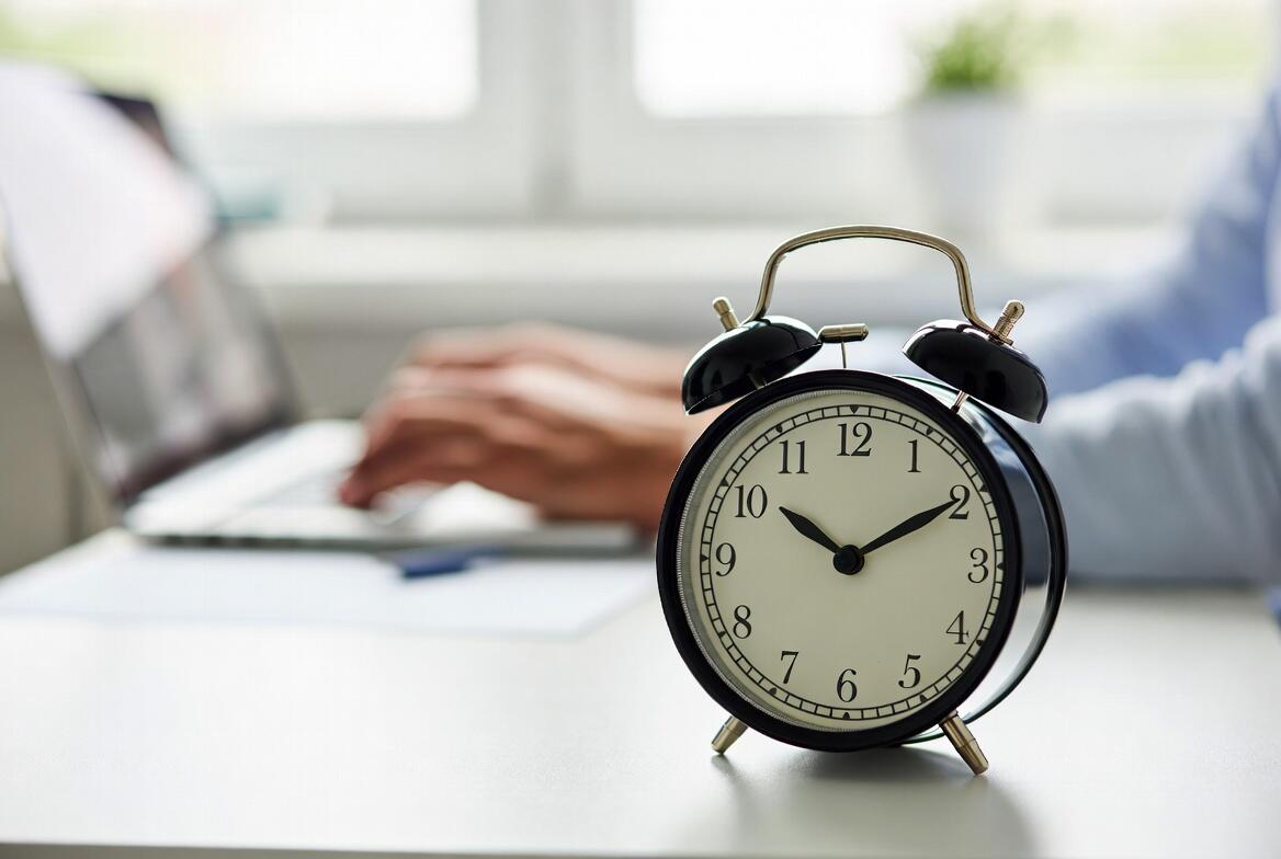 mani che digitano su tastiera con in primo piano una sveglia